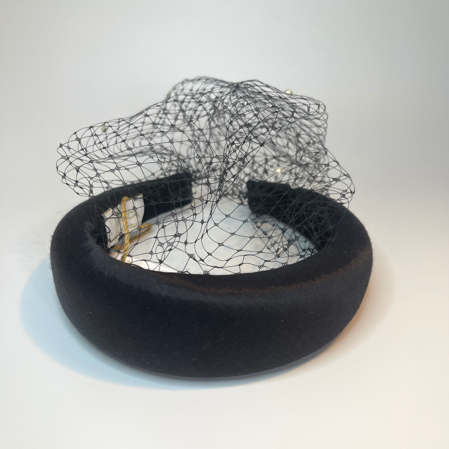 black satin covered padded headband with an attached veil that is studded with faux pearls.