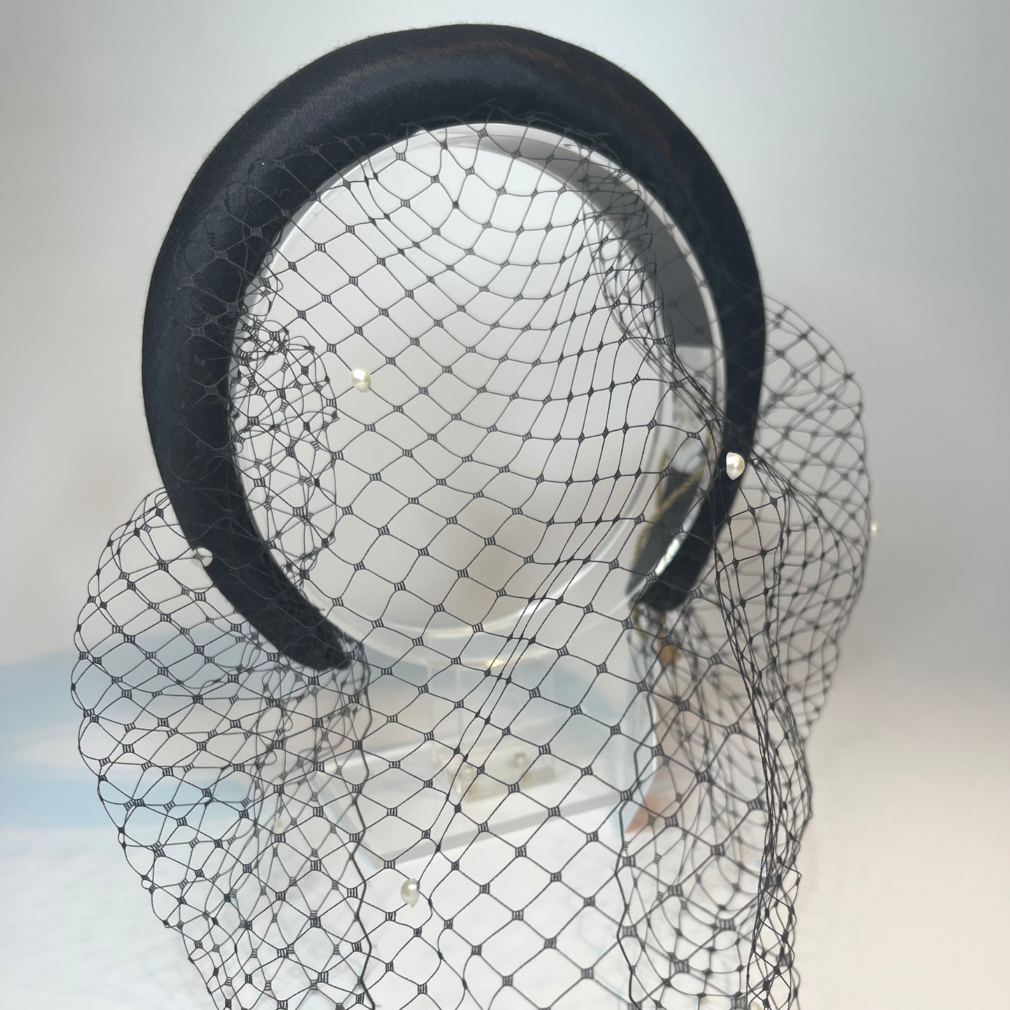 black satin covered padded headband with an attached veil that is studded with faux pearls.