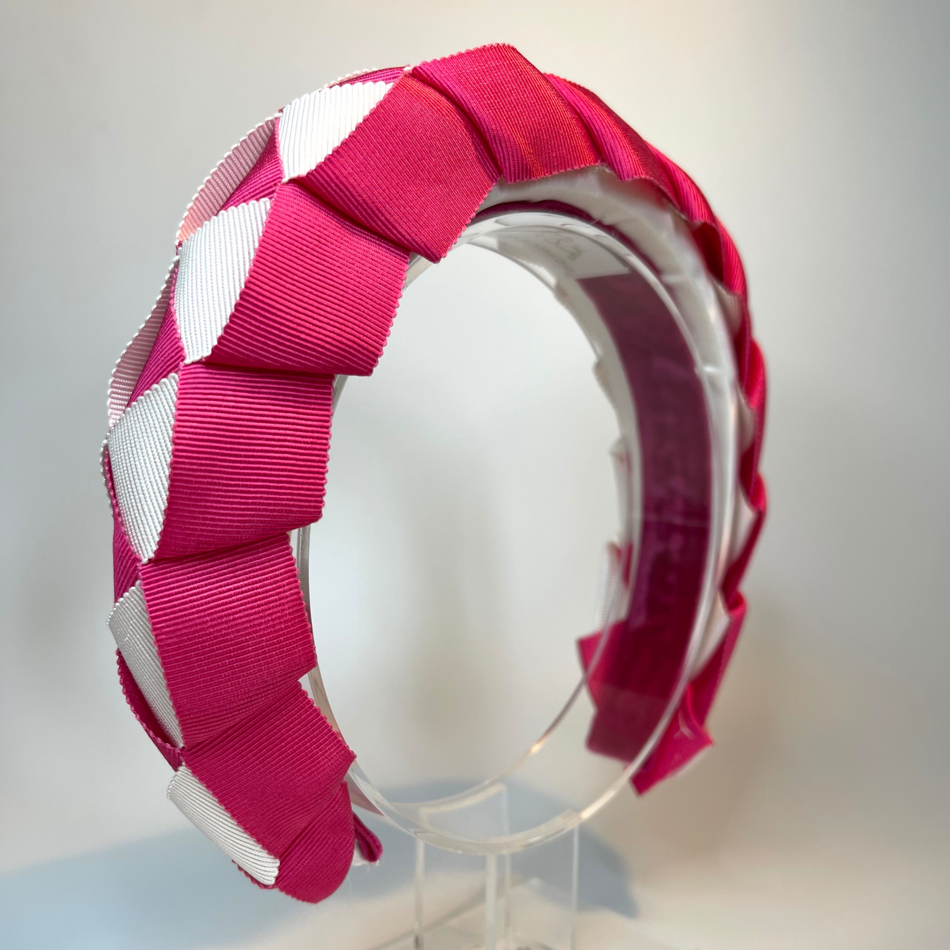 Pink and white woven ribbon sitting on a white satin padded headband, lined in velvet.